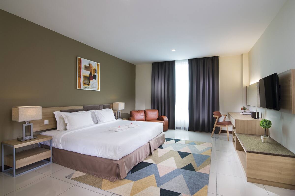 Una habitación de hotel moderna con una cama grande, un escritorio, un televisor y una ventana con cortinas.