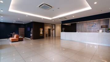 A modern hotel lobby with a reception desk, seating area, and a large mirror.