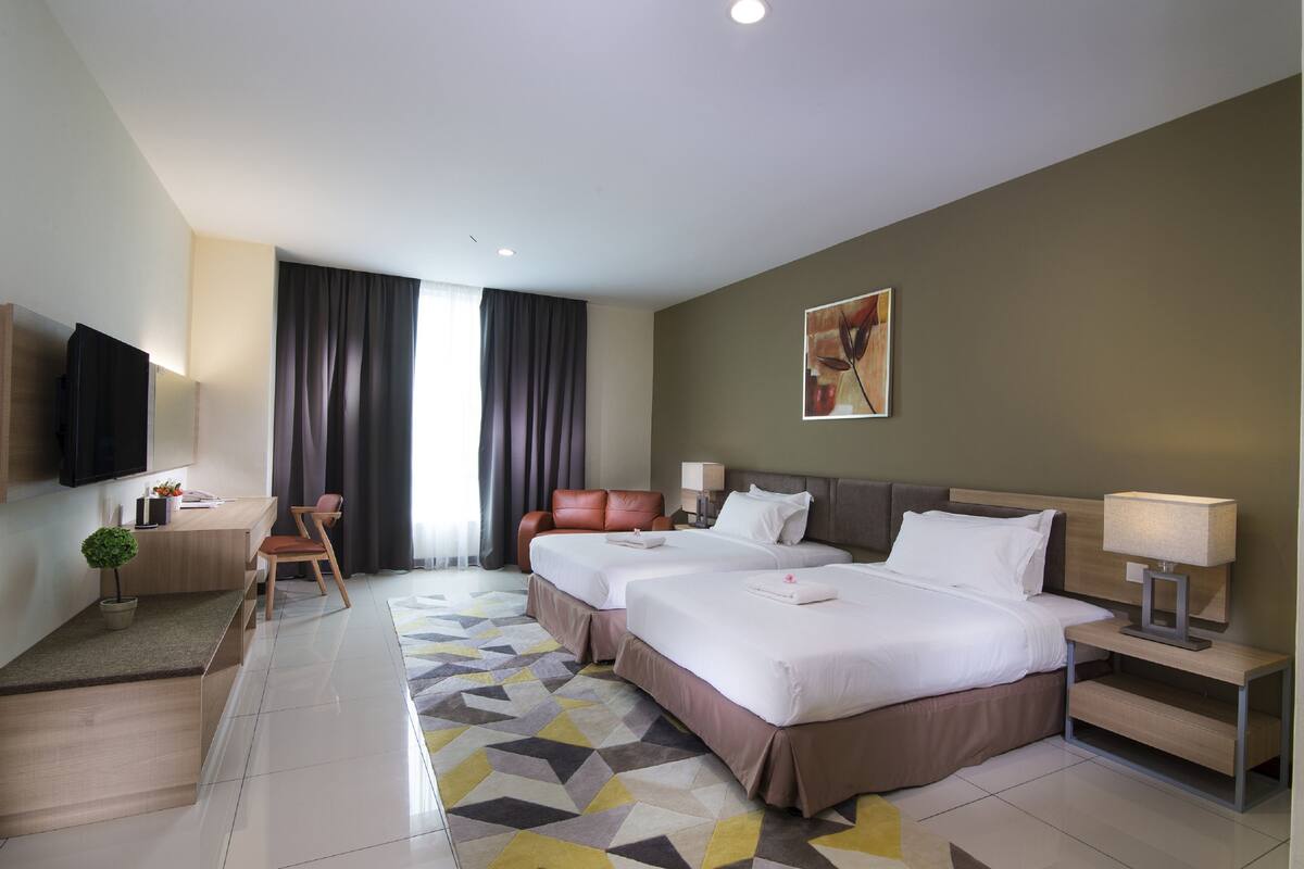 Habitación de hotel con dos camas, un escritorio, un televisor y un ventanal grande con cortinas.