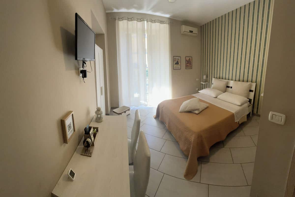 Une chambre d’hôtel comprenant un lit, un bureau, une chaise, un téléviseur fixé au mur et une fenêtre avec des rideaux.