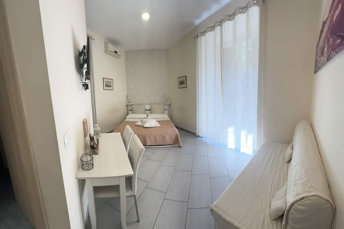 Une chambre d’hôtel avec un lit, une petite table avec des chaises, un canapé et une fenêtre avec des rideaux.