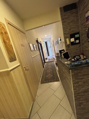 A hallway with a wooden door, a framed picture, a rug, a desk with a computer, and a stone wall. - B&B 248 (Naples)