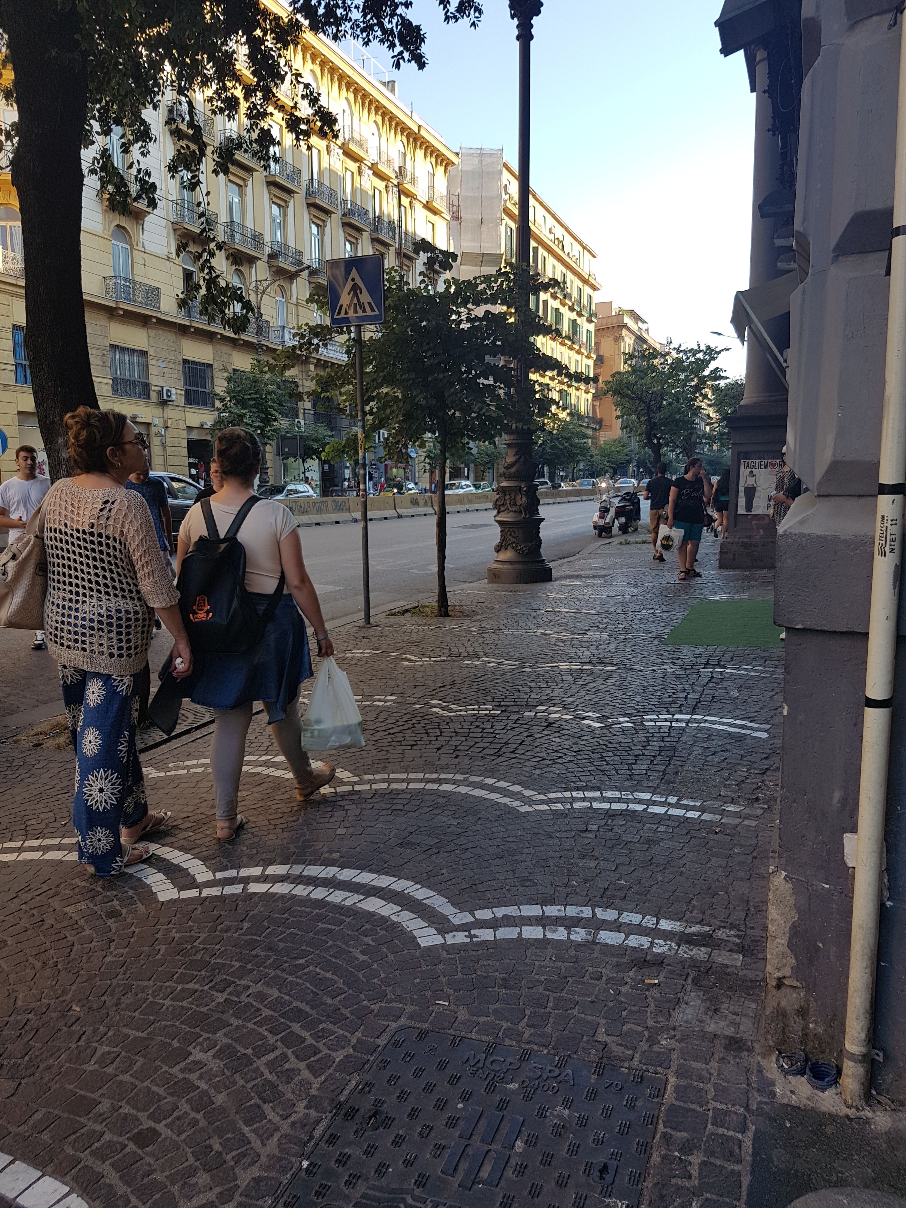 A cobblestone street with pedestrians, a tree, and a building with balconies.
