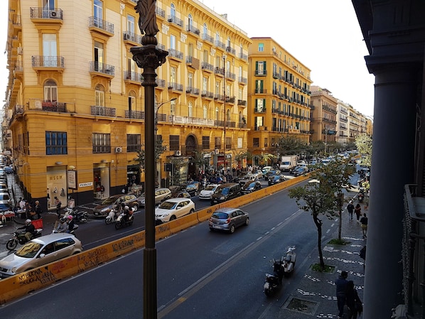 A busy urban street with yellow buildings, parked cars, and motorcycles.