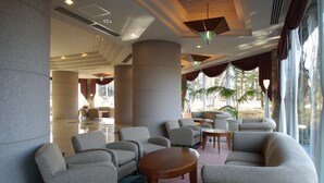 A lobby with a seating area, large pillars, and a view of palm trees through large windows.