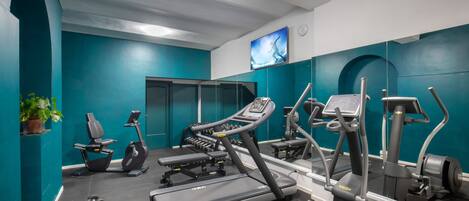 A gym with various exercise equipment, teal walls, and a large mirror.