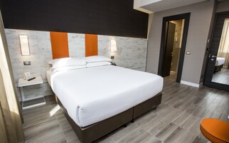 Et moderne hotelværelse med en stor seng, sengeborde, et spejl og et badeværelse, der kan ses igennem en åben dør.