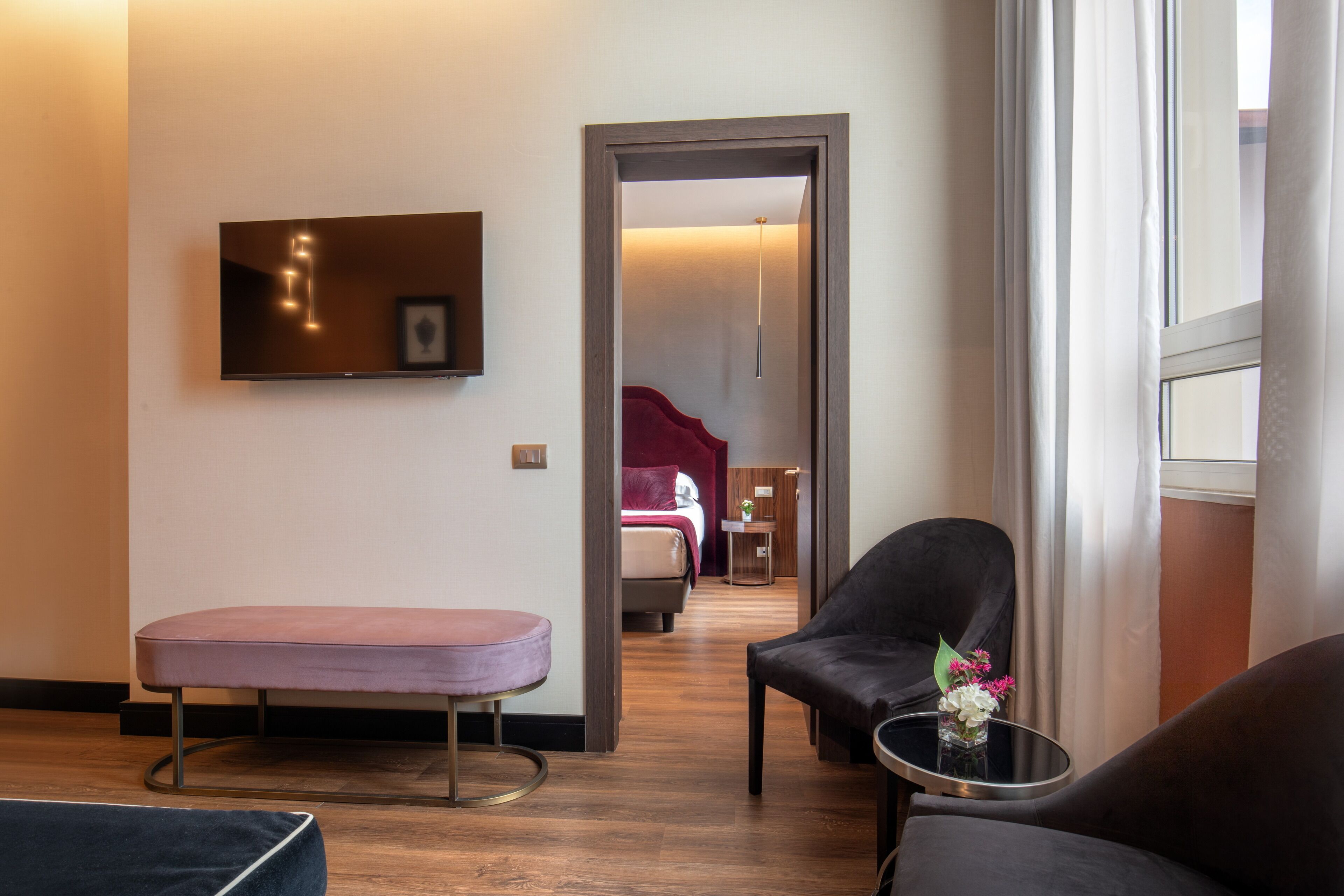 Une chambre d’hôtel comprenant un lit, un coin salon avec un fauteuil et une petite table, un banc et un téléviseur fixé au mur.