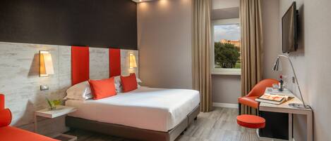 A modern hotel room with a large bed, a desk with a chair, a TV mounted on the wall, and a window with curtains.