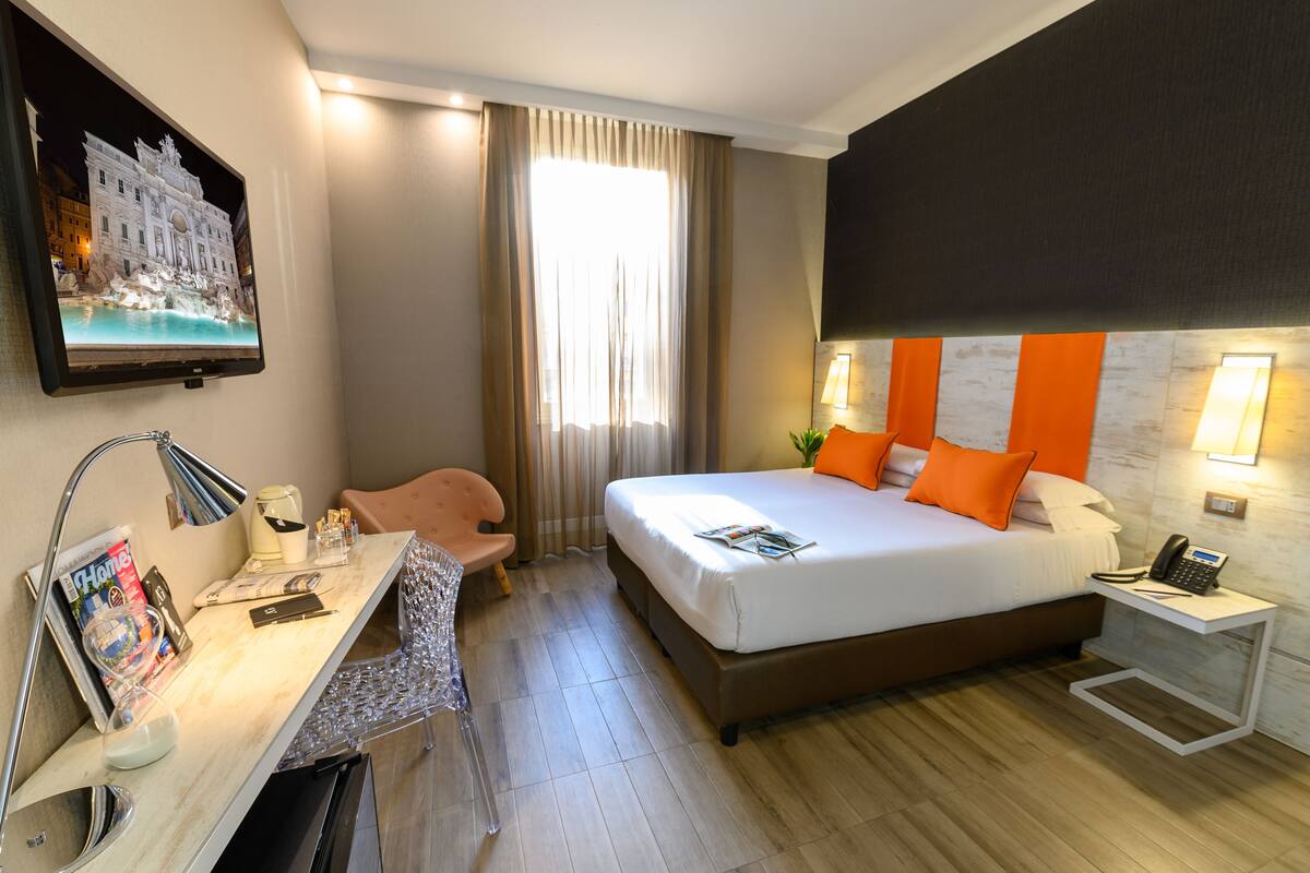 A hotel room with a bed, desk, chair, and a painting of a building.