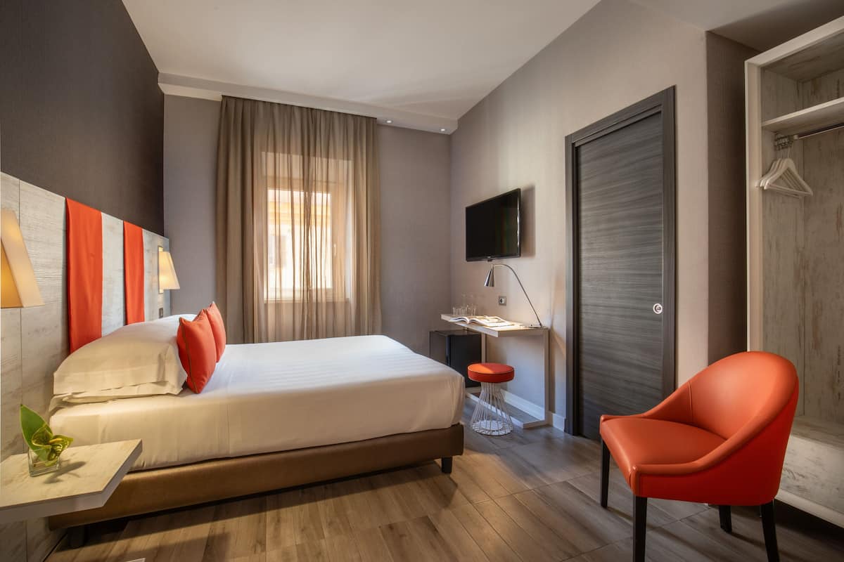 A modern hotel room with a bed, a desk, a TV, and a wardrobe.