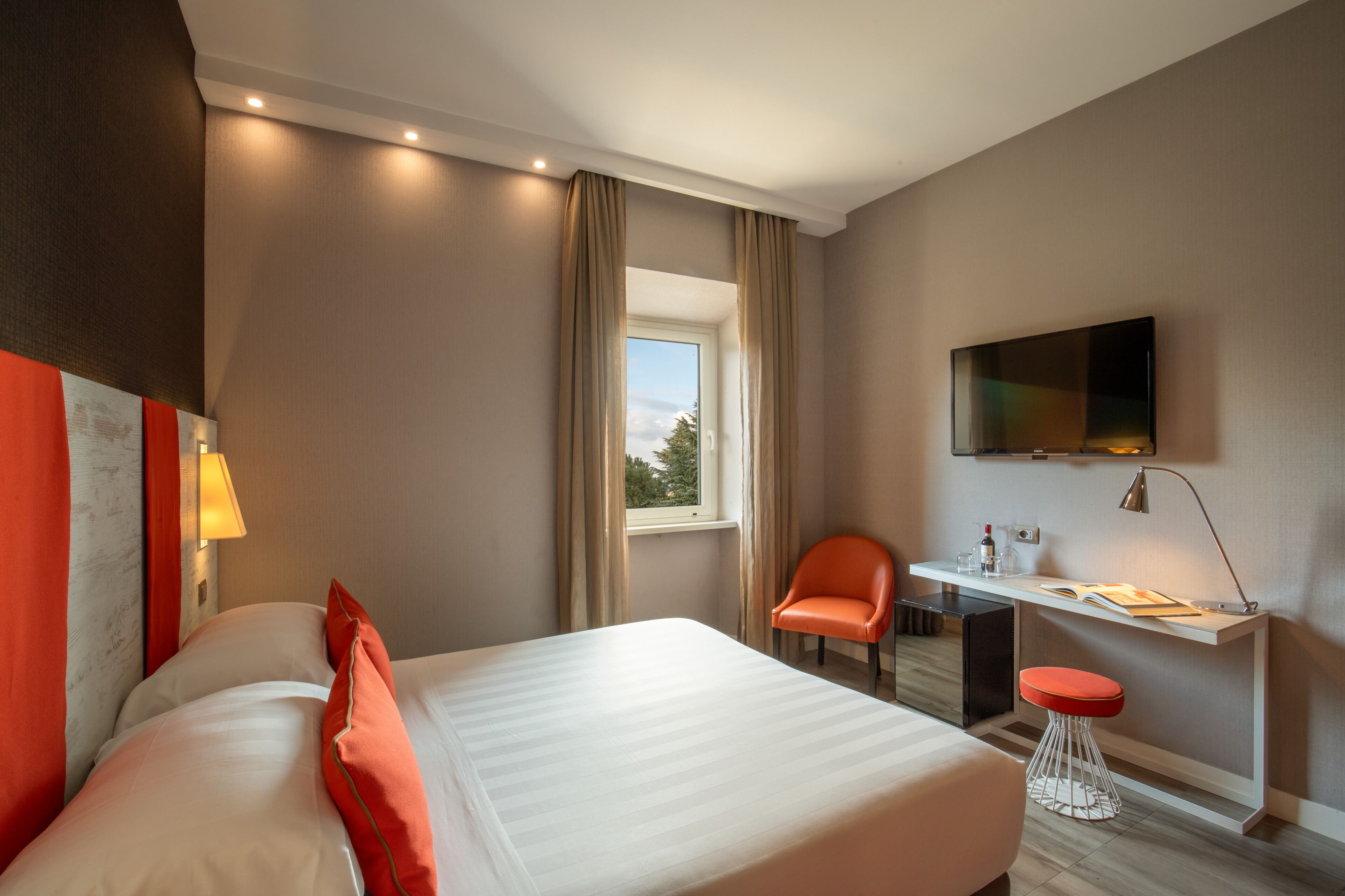 A hotel room with a bed, a desk, a chair, a TV, and a window.