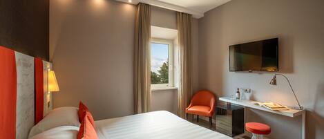 A hotel room with a bed, a desk, a chair, a TV, and a window.