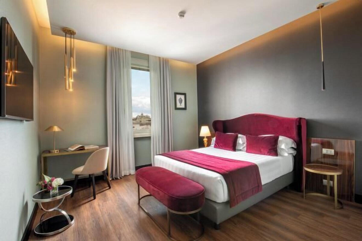 Una habitación de hotel con una cama grande, un escritorio, una silla, una mesita y una ventana.