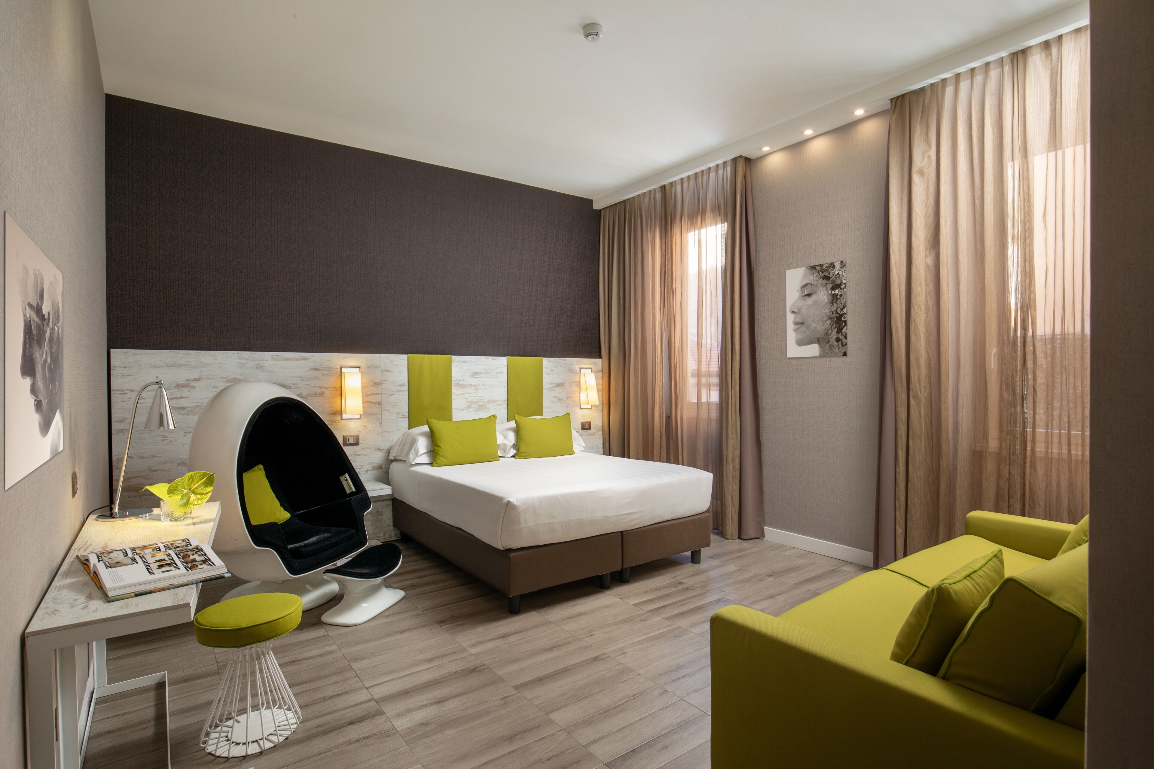 Una habitación de hotel moderna con una cama grande, un escritorio con una silla, un sofá y un ventanal con cortinas.