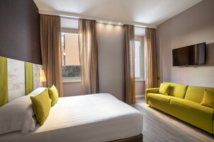 A hotel room with a bed, a sofa, a TV, and large windows with curtains.