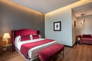 A modern hotel room with a large bed, a bedside table with a lamp, a small side table, and a sofa.