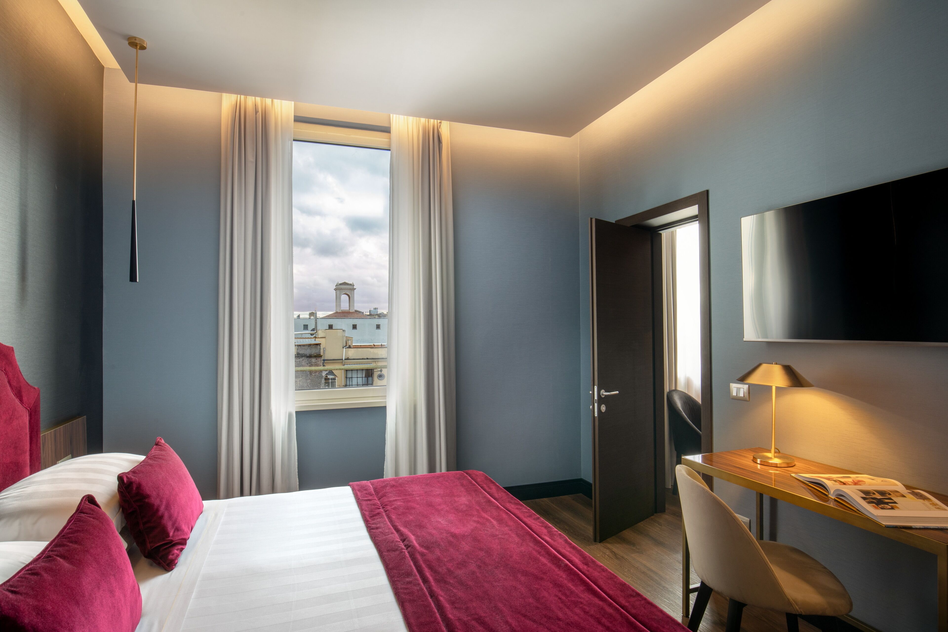 A hotel room with a bed, a desk, a chair, a TV, and a window with curtains.