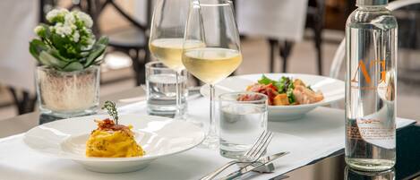 A dining table set with plates of food, glasses of white wine, and a water bottle.