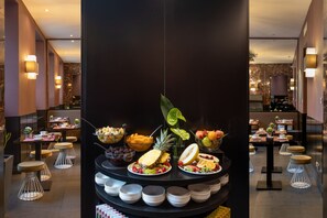 A buffet area with various fruits and dishes, surrounded by modern seating and a dark-toned interior.