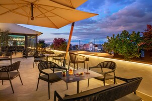 An outdoor seating area with tables and chairs, a bar, and a view of the cityscape.