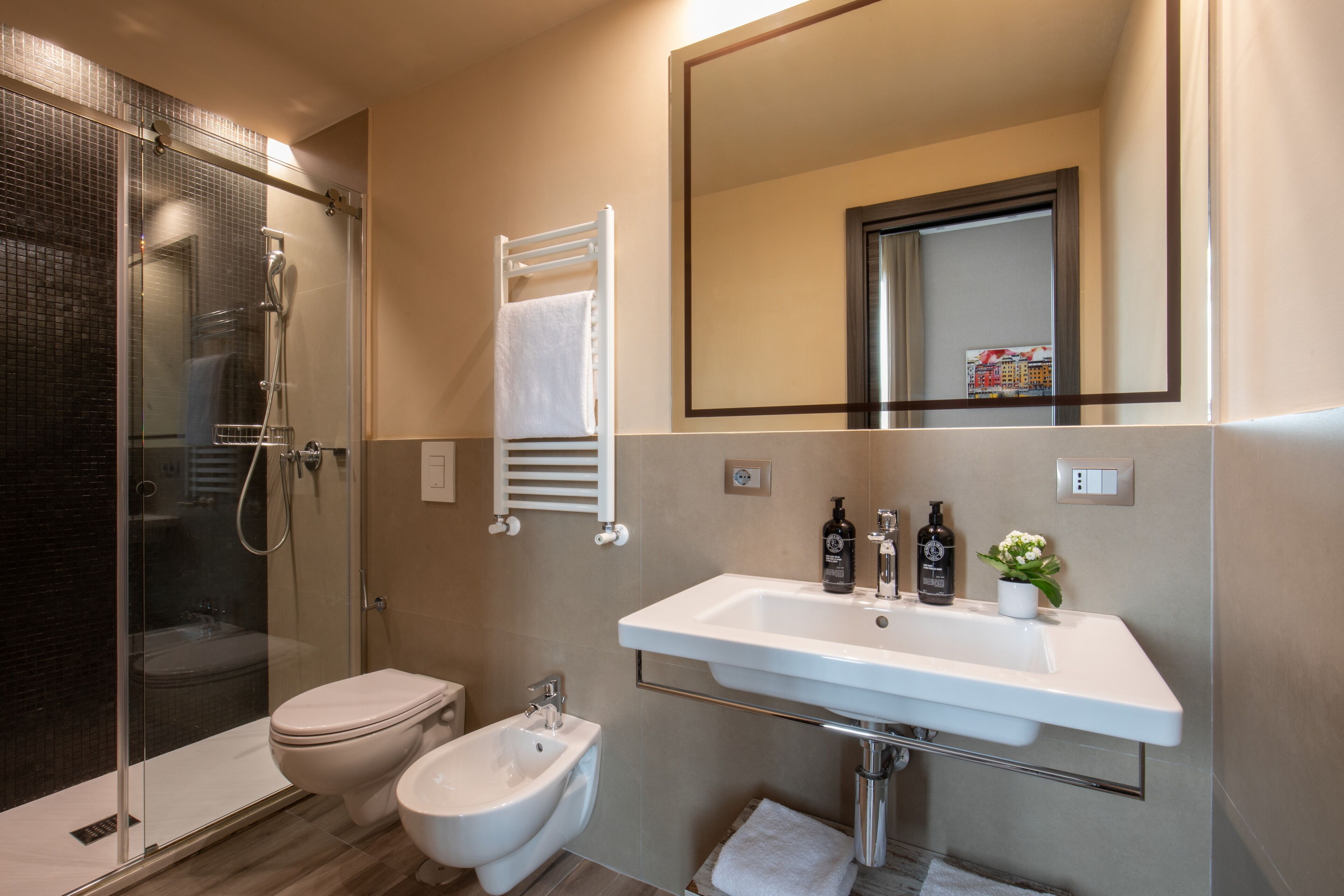 A modern bathroom with a glass-enclosed shower, a toilet, a bidet, and a sink with toiletries.