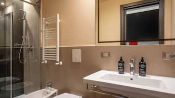 Et moderne badeværelse med en brusekabine med glasdøre, en hvid vask med tre shampoo-flasker og et hvidt toilet.