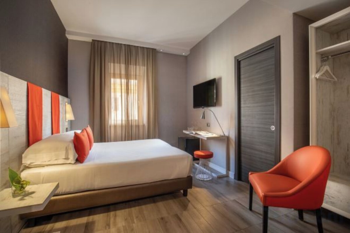 A hotel room with a bed, a desk, a chair, a TV, and a wardrobe.