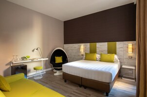 A modern hotel room with a bed, a desk, a chair, and a sofa.
