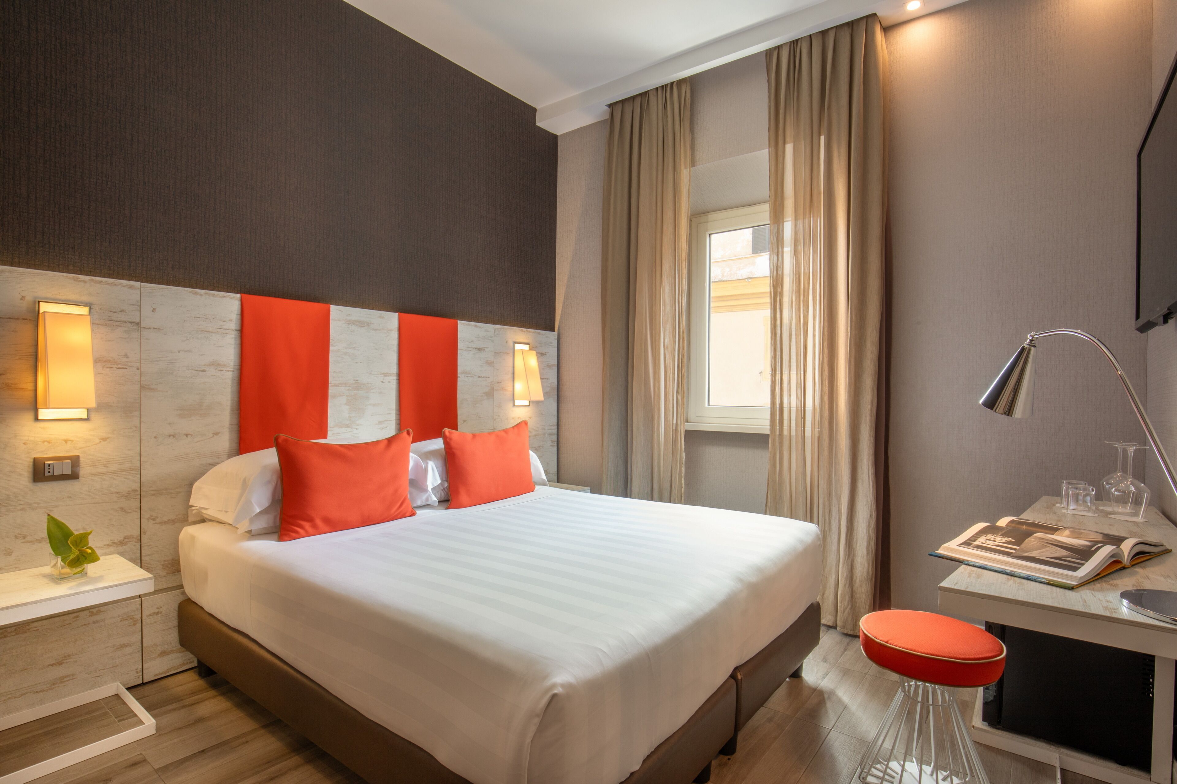 Una habitación de hotel moderna con una cama grande, un escritorio con lámpara y una ventana con cortinas.