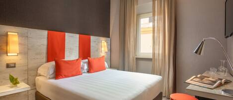 Una habitación de hotel moderna con una cama grande, un escritorio con lámpara y una ventana con cortinas.