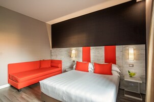 Una habitación de hotel moderna con una cama grande, un sofá rojo y una mesita de noche con una lámpara.