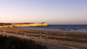 Una playa con arena, una valla de madera y un acantilado al fondo.