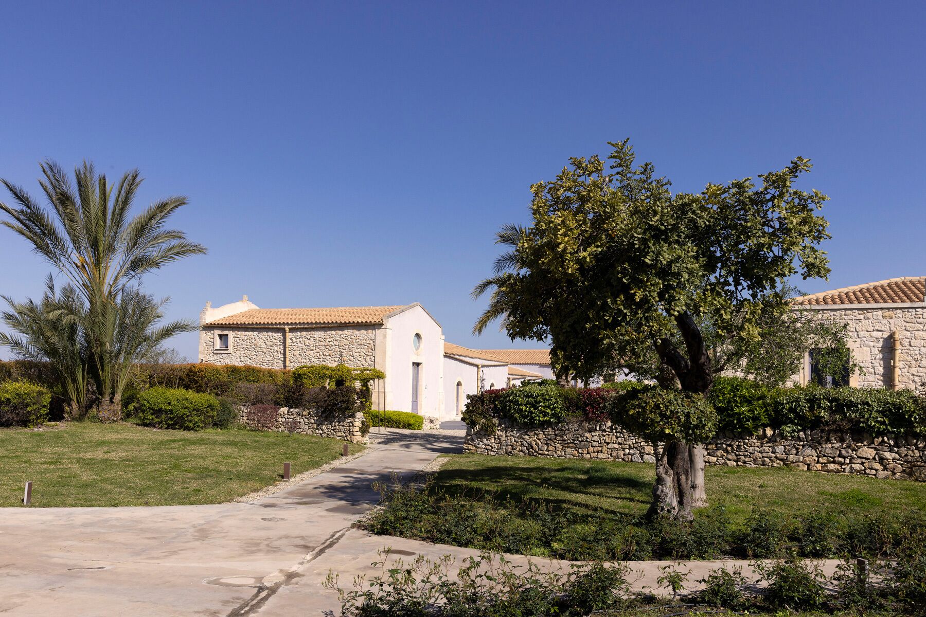 A pathway leading to a building with stone walls and a tiled roof.