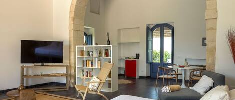 A spacious living area with a large bed, a television, a bookshelf, and a dining area with a table and chairs.