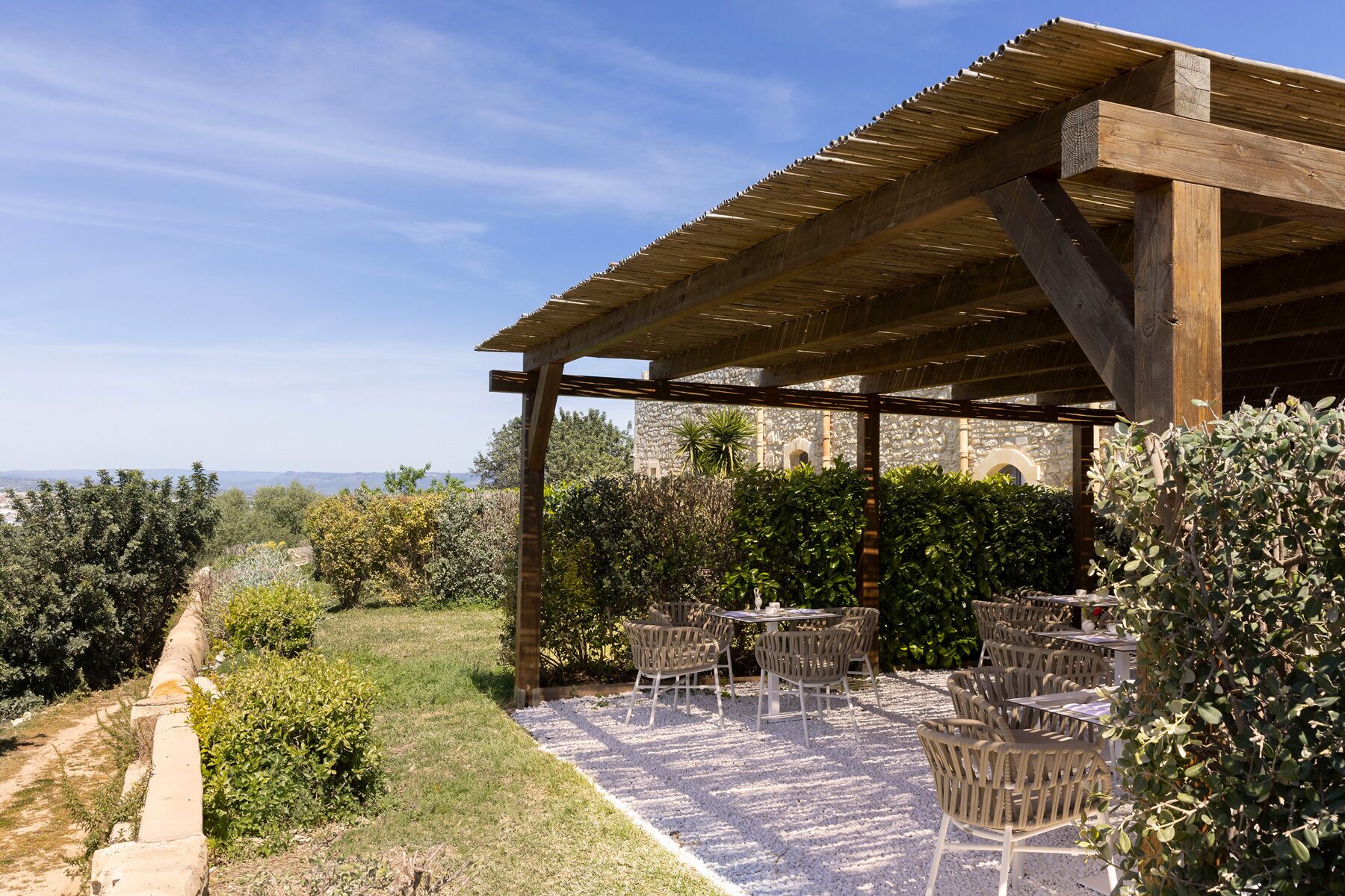 An outdoor patio with tables and chairs, a stone wall, and a view of the landscape.