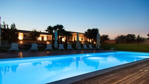 Una piscina con sillones de playa y sombrillas, rodeada de una terraza de madera y muros de piedra.