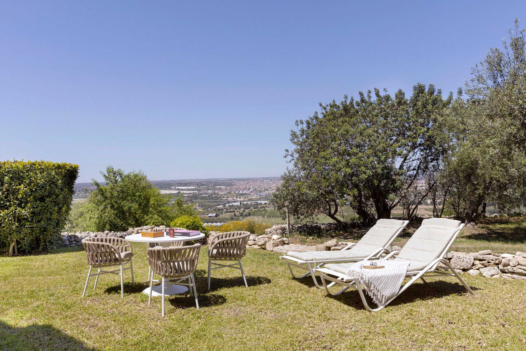 Una terraza con mesa y sillas, sillones de descanso y vistas a un paisaje urbano.