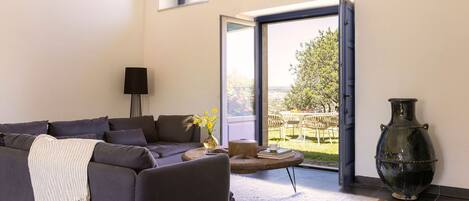 Una sala de estar moderna con un sofá gris oscuro, un jarrón grande y vistas a un patio exterior.
