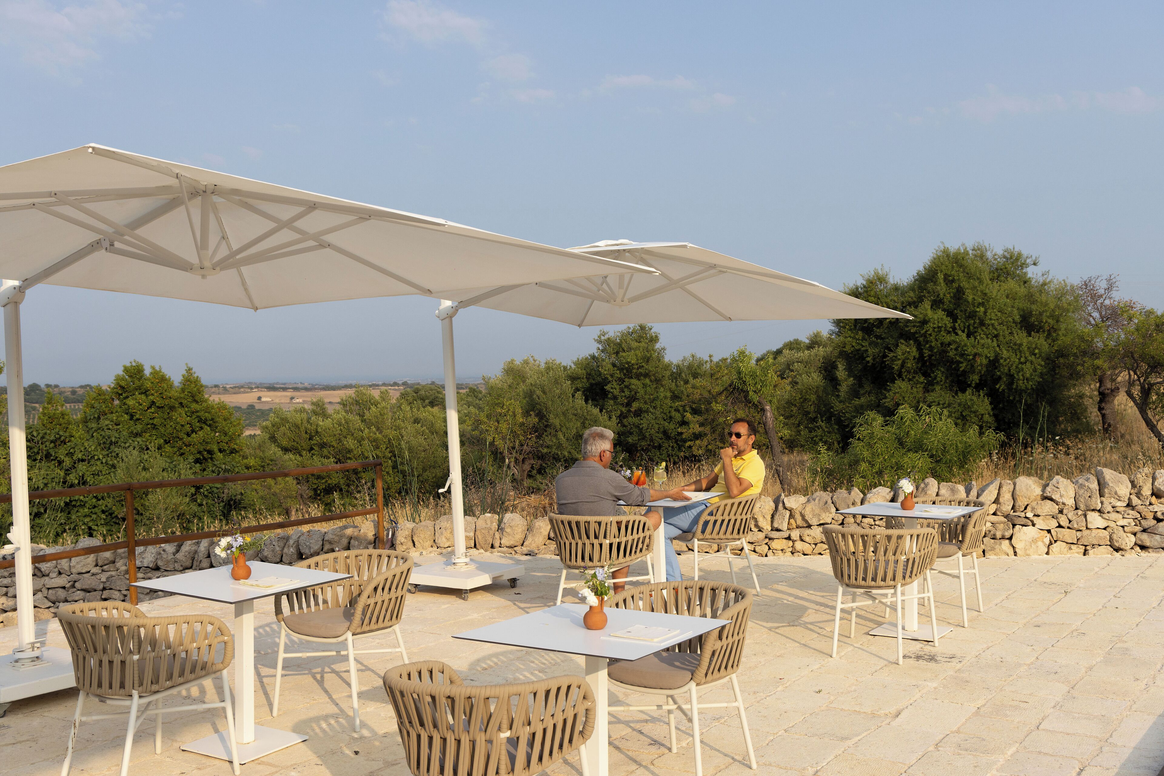 An outdoor seating area with tables and chairs under umbrellas, overlooking a scenic landscape.