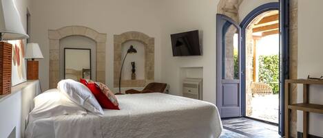 A bedroom with a large bed, a TV, and a view through an open door to an outdoor area.