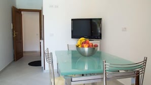 A dining area with a glass table, metal chairs, a bowl of fruit, and a mounted television. - Agriturismo L'Oasi (Ceraso)