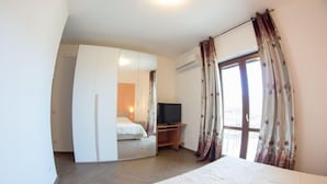A bedroom with a bed, a TV, a wardrobe, and a window with curtains. - Agriturismo L'Oasi (Ceraso)