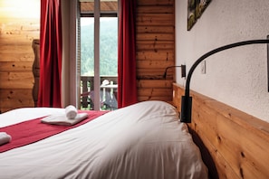 Una habitación tipo cabaña de madera con cama, cortinas rojas y vistas a un área boscosa.