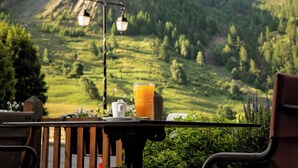 A mountain view with a table set for a meal, including a glass of orange juice and a cup, overlooking a valley. - Hôtel Castillan (La Grave)