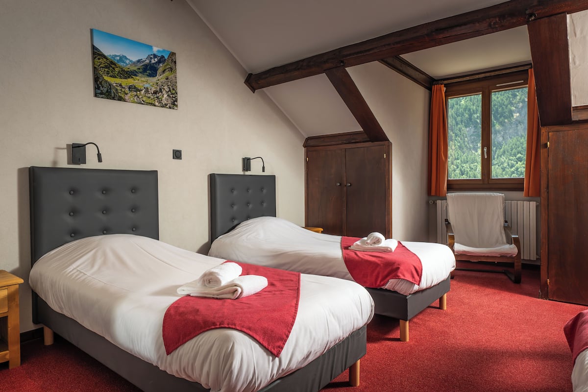 A bedroom with two beds, a wooden chair, a radiator, and a window with curtains.