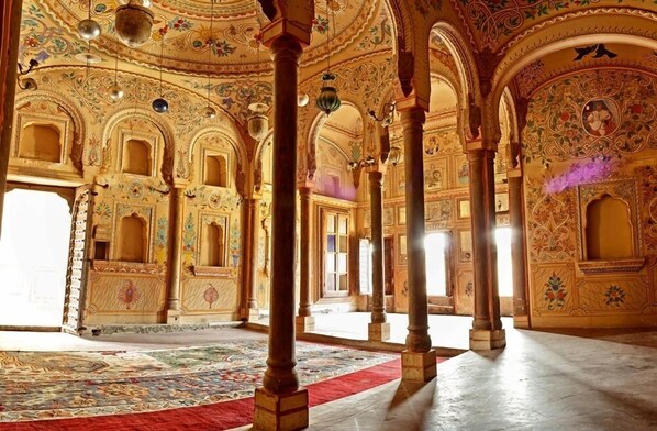 An ornate interior with intricate architectural details, including arches and columns, and a patterned carpet. - Vivaana Culture Hotel (Churi Ajitgarh)