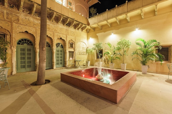 A courtyard with a central water feature, arched doorways, and potted plants. - Vivaana Culture Hotel (Churi Ajitgarh)