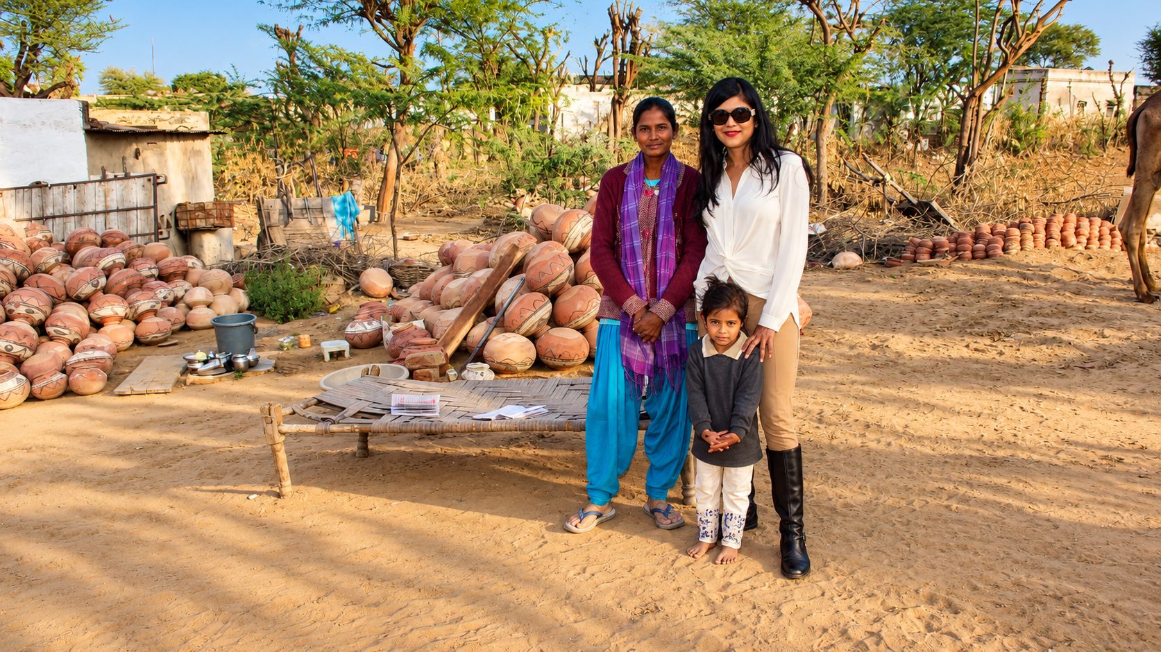 A group of people standing in a sandy outdoor area with pottery and a woven mat.