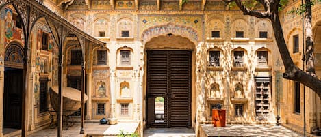 Un patio con una puerta grande y ornamentada, plantas en macetas y detalles arquitectónicos tradicionales.